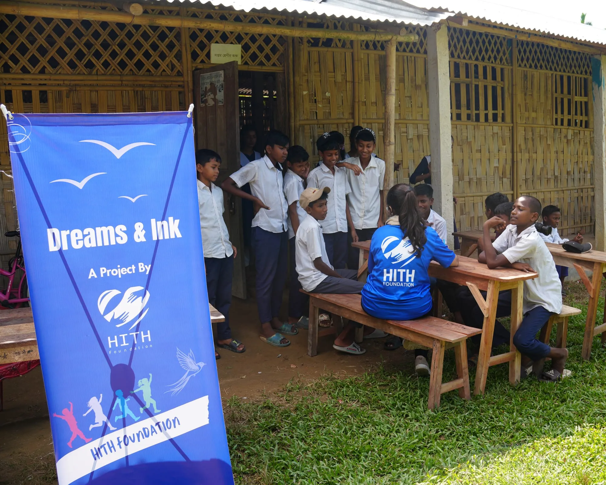 Students gather outside their bamboo school beside the Dreams & Ink banner