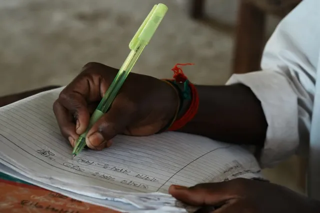 A child's hand writing Bengali script in an exercise book