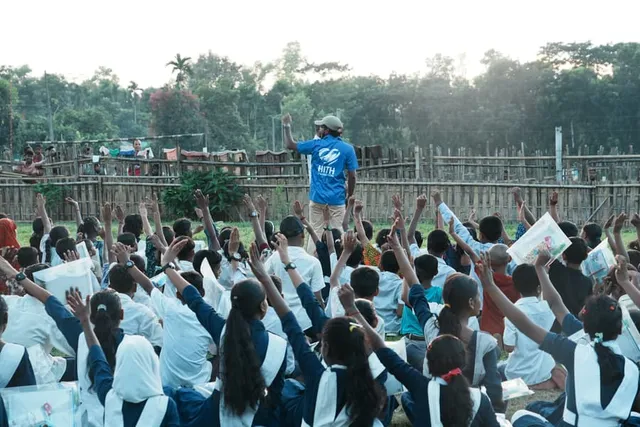 A volunteer leads the crowd of children, hands raised