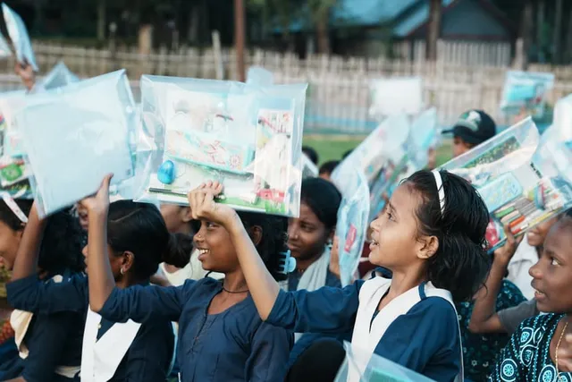 Schoolgirls hold their new supply kits above their heads