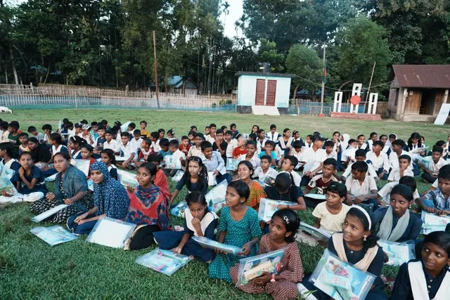 Children with supply packets seated on the field at dusk