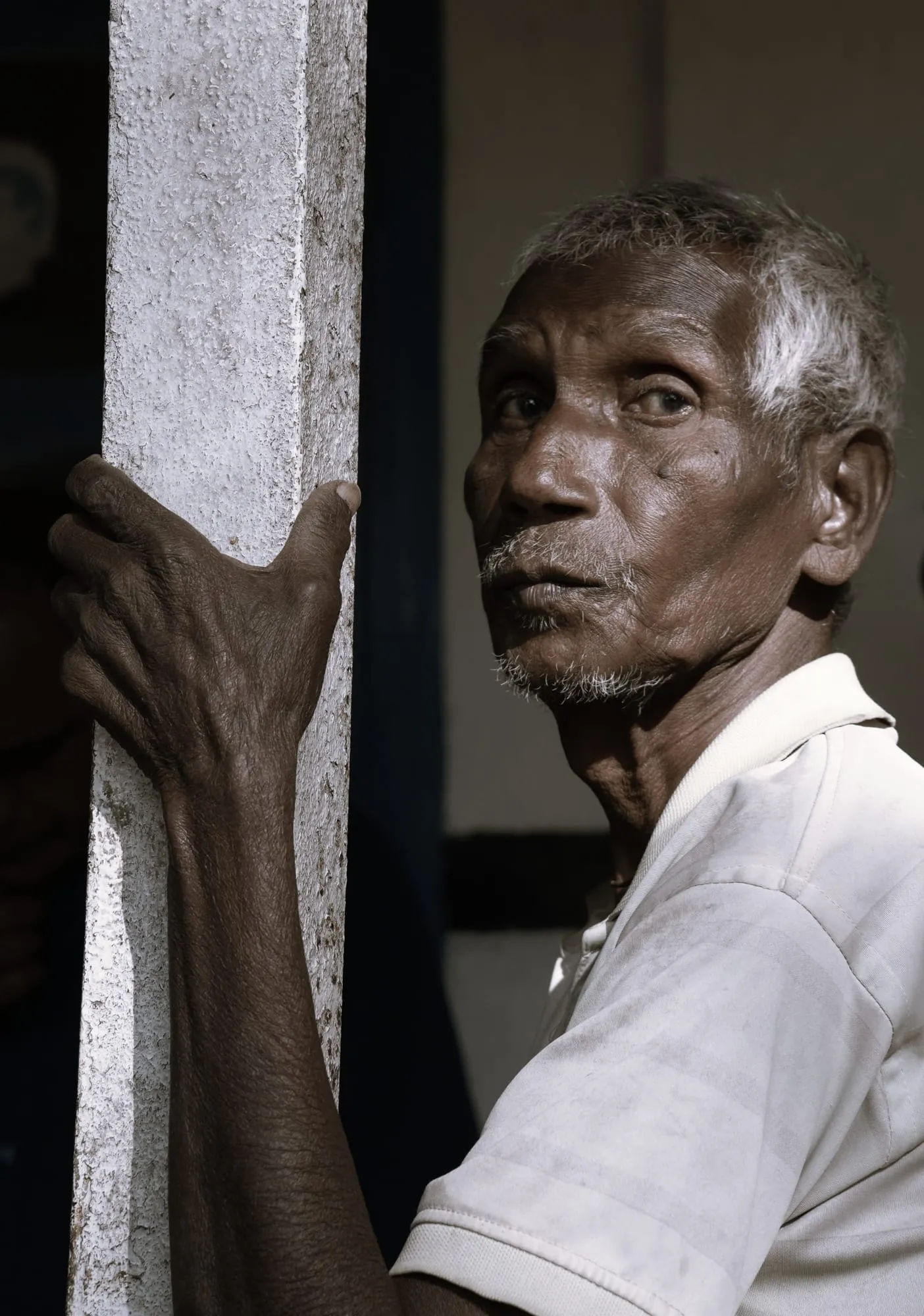 An elder tea worker looking back, his hand resting on a post